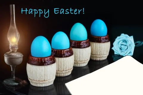 Blue Easter eggs, a lit old lamp and a blank sheet of paper on a black backgr 스톡 사진