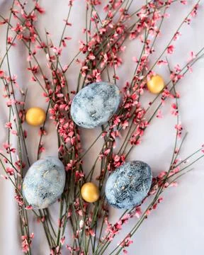 Blue easter eggs with small golden chocolates on pink flower background. Stock Photos