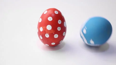 Blue egg with pattern hits red chicken egg with polka dots on white table Stock Footage 300686797