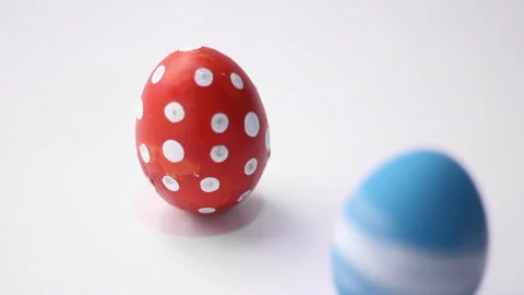 Blue egg with spins and hits red chicken egg with polka dots on white table Stock Footage 268349986