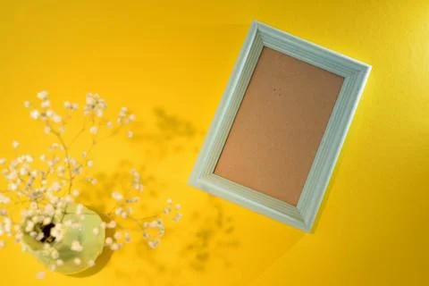 Blue empty photo frame on yellow background with vase and flower mockup Space Stock-Fotos