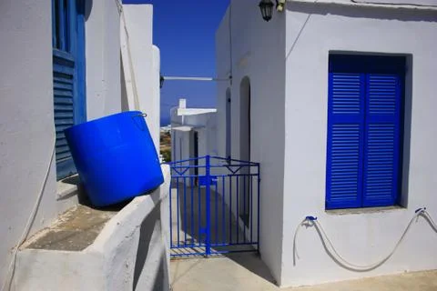 Blue empty plastic carrying barrel and little steel door by white island houses Stock Photos