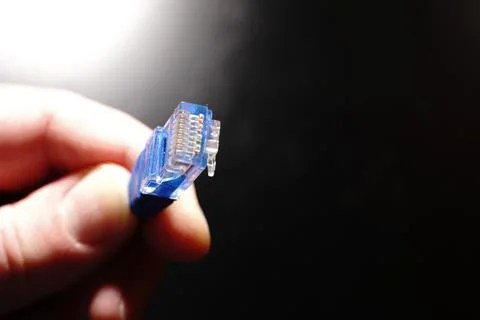 A blue ethernet internet cable in your hand on a black background. Copyspace Stock Photos