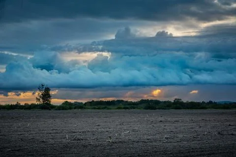 Blue evening cloudy sky over a plowed field Stock Photos