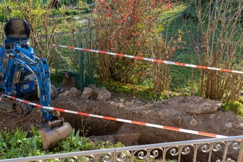 Blue excavator between temporary red and white tape barrier in back yard. Foto stock
