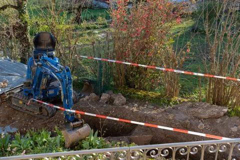 Blue excavator between temporary red and white tape barrier in back yard. Foto stock