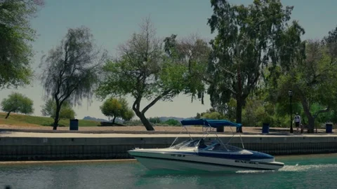 Blue Excel ski boat passes by tree-lined desert park in an Arizona lake cana Stock Footage 241498538