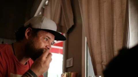 Blue-eyed hipster guy with a beard and a cap snapback eating a sandwich.4k video Stock Footage 109692042