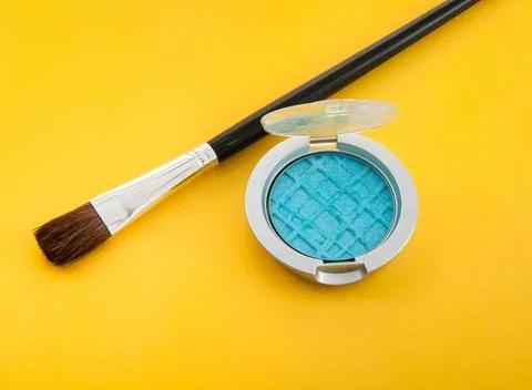 Blue eyeshadow compact and brush on a vibrant yellow background Stock Photos