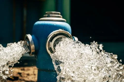 Blue fire hydrant flushing high-pressure water from open side valves into s.. Stock Photos