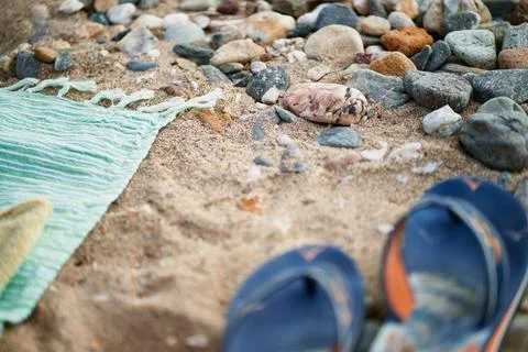 Blue flip flops and a beach towel lying on sandy ground with pebbles 스톡 사진