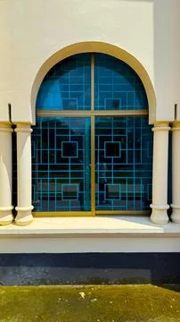 Blue geometric pattern window displays reflections between two white pillars  스톡 사진