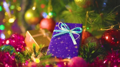 A blue gift box with bow on a blurred background of festive tinsel, gold sequins Stock Footage 322105710