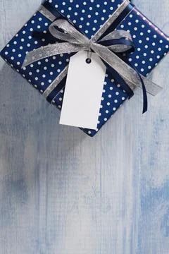 The blue gift box is tied with a silver-dark blue ribbon. An empty white tag  Stock Photos