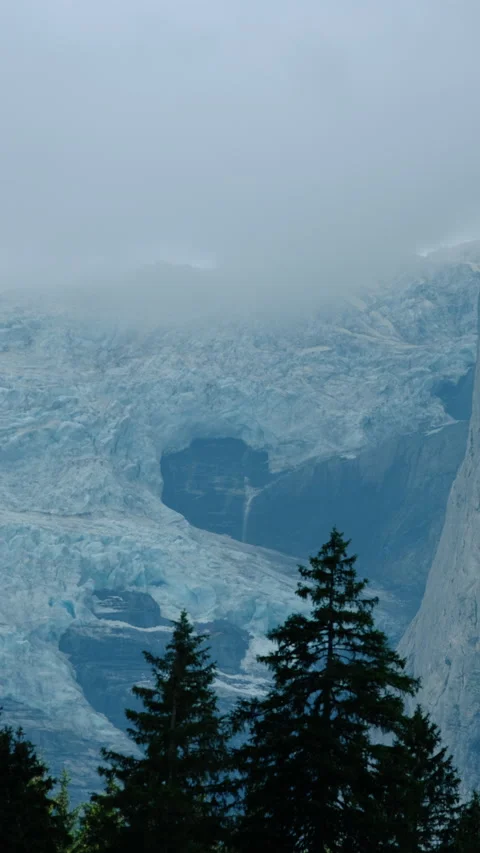 A blue glacier with a water stream on the wall of a rocky mountain with clouds a Stock Footage 284617448