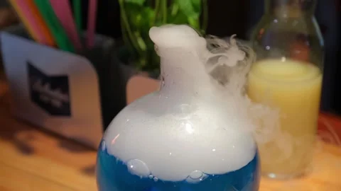 Blue glass flask emitting white vapor on wooden surface indoors Video stock 342070867