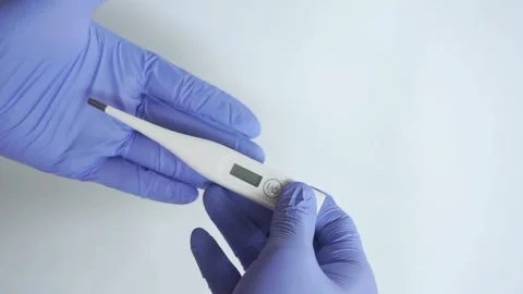 Blue gloved hand holds digital thermometer, clinical background Stock Footage 322633449