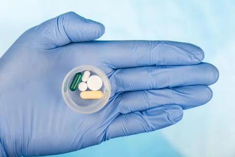 Blue-gloved hand pulls a dose of pills Stock Photos