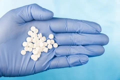 Blue-gloved hand pulls a handful of white pills Stock Photos