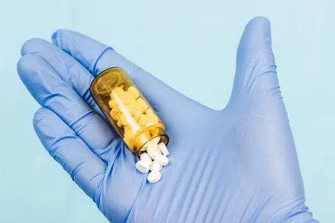 Blue-gloved hand pulls a jar of pills Stock Photos