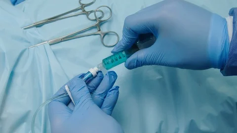 Blue Gloved hands use a syringe to inject teal liquid into a tube or IV tubing Video stock 103283518