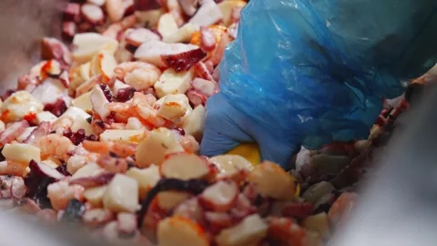 A blue-gloved worker scoops chopped mixed seafood from a metal container with a Stock Footage 348089331