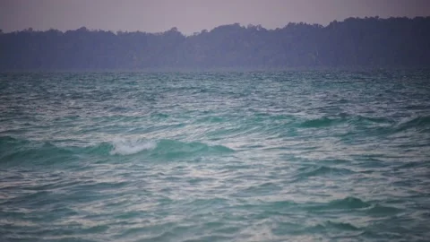 Blue green water waves lapping at shore with dark trees in the distance of Stock Footage 170014158