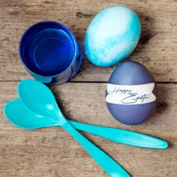 Blue greeting card with easter eggs, egg spoons and egg dyes, text happy east 스톡 사진