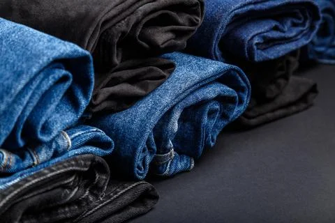 Blue jeans folded in rolls lie on black background. Black and blue denim pants Stock Photos