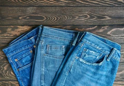 Blue jeans in a row, stack of denim pants, composition on wooden background w Stock Photos