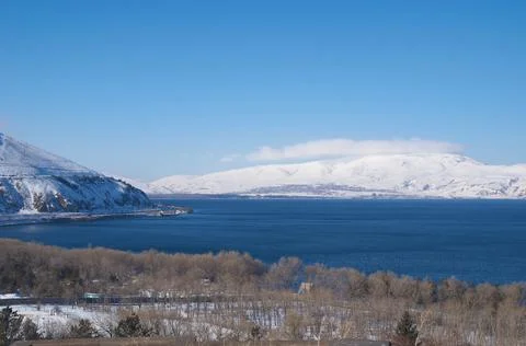 Blue Lake Sevan on the background of snow-capped mountains on a sunny day Stock Photos