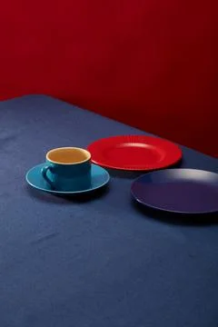 A blue leather dining table with plates and cups on a red background Foto stock
