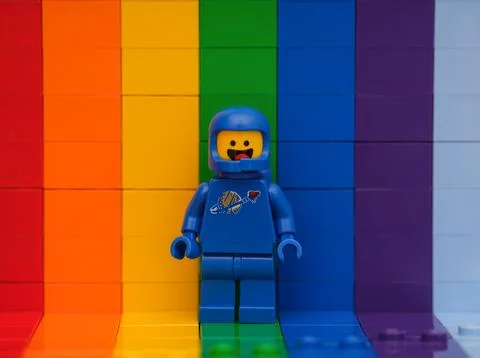 A Blue Lego astronaut Benny minifigure standing against a rainbow backdrop Hi Res 230228843