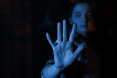 Blue light illuminates a hand held in front of a dark window Stock-Fotos