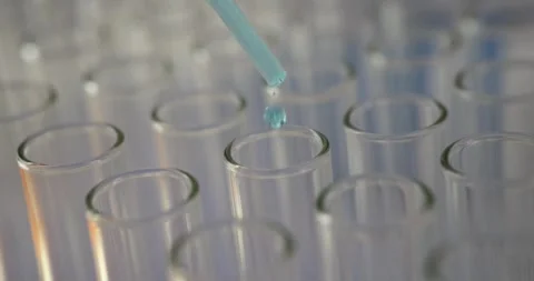 Blue liquid droplets fall from pipette into glass test tubes Stock Footage 312930038