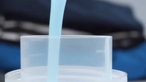 Blue liquid laundry detergent is poured into a palstic measuring cap Stock Footage 152618073
