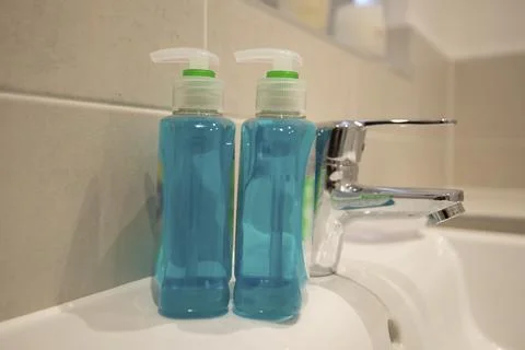 Blue liquid soap bottles stand beside a sink Stock Photos