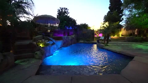 Blue lit lagoon pool with rock waterfall in a garden at dusk Stock Footage 345538755