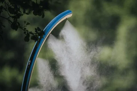 Blue misting system nozzle releasing fine water vapor in a lush green outdo.. Stock Photos