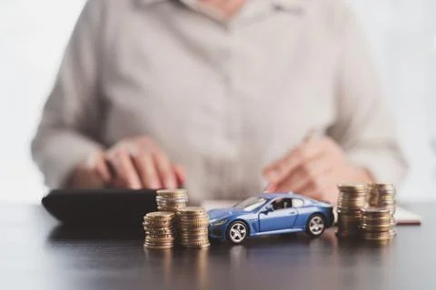 Blue model car positioned between coin stacks while a person calculates exp.. Stock Photos