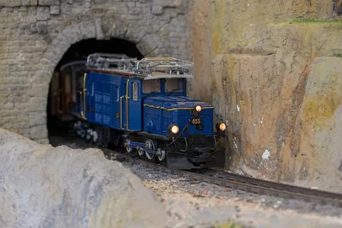 Blue model train exits stone tunnel during daytime model railroad operation Stock Photos