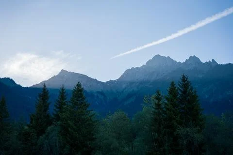 Blue Mountain Range and Pine Forest Silhouette at Dusk With Contrail in Cle.. Stock Photos