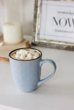 Blue mug with cocoa, coffee, marshmallows on white table with decor Stock Photos