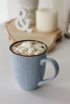Blue mug with cocoa, coffee, marshmallows on white table with decor Stock Photos