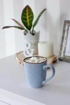 Blue mug with cocoa, coffee, marshmallows on white table with decor Stock Photos