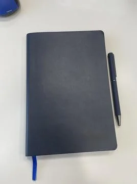 A blue notebook on a clean white surface with a navy blue pen Stock Photos