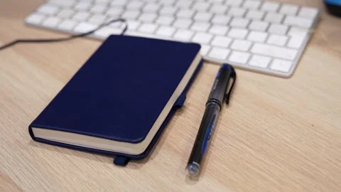 Blue Notebook Pen and Computer Keyboard on Wooden Office Desk Stock Footage 332545778
