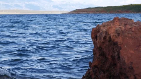 Blue ocean water ripples gently beside a rugged reddish rock Stock Footage 337410756
