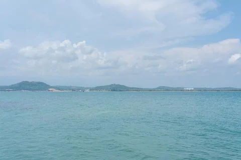 Blue ocean water stretching to distant green hills under a bright summer Stock Photos
