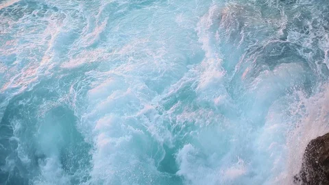 Blue ocean waves break against rocky cliffs of the shore Stock Footage 130116818